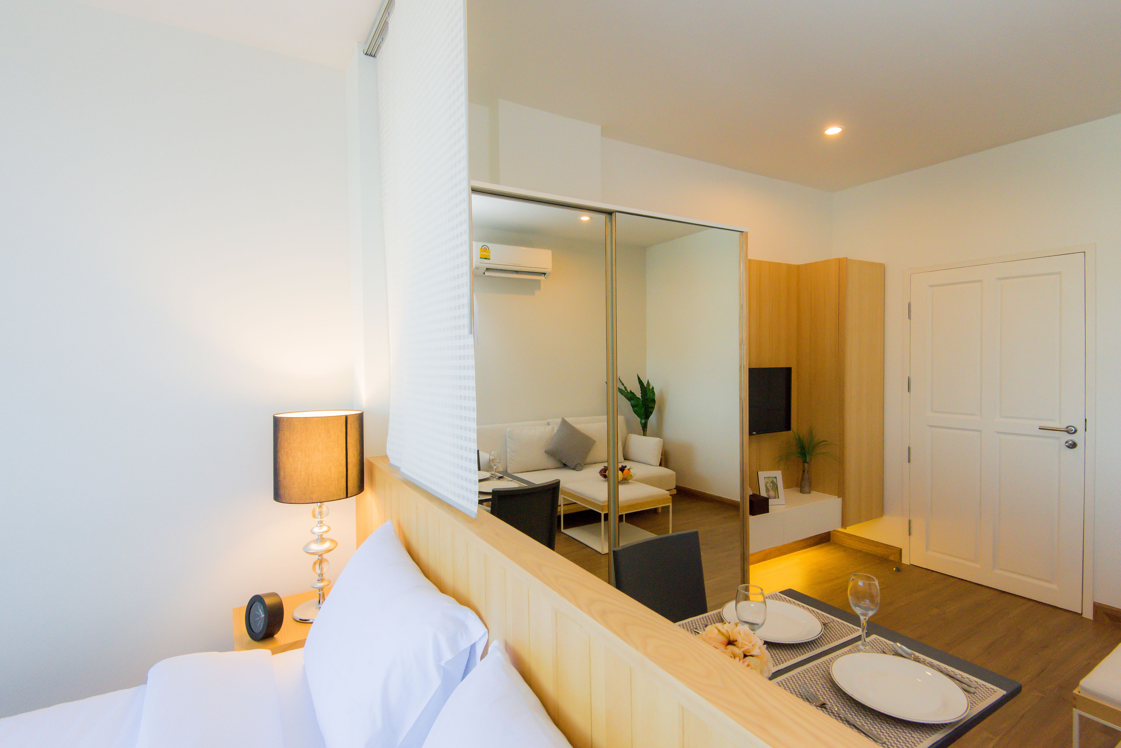 Habitación de hotel con cama, mesita de noche, lámpara y zona de comedor con mesa para dos.
