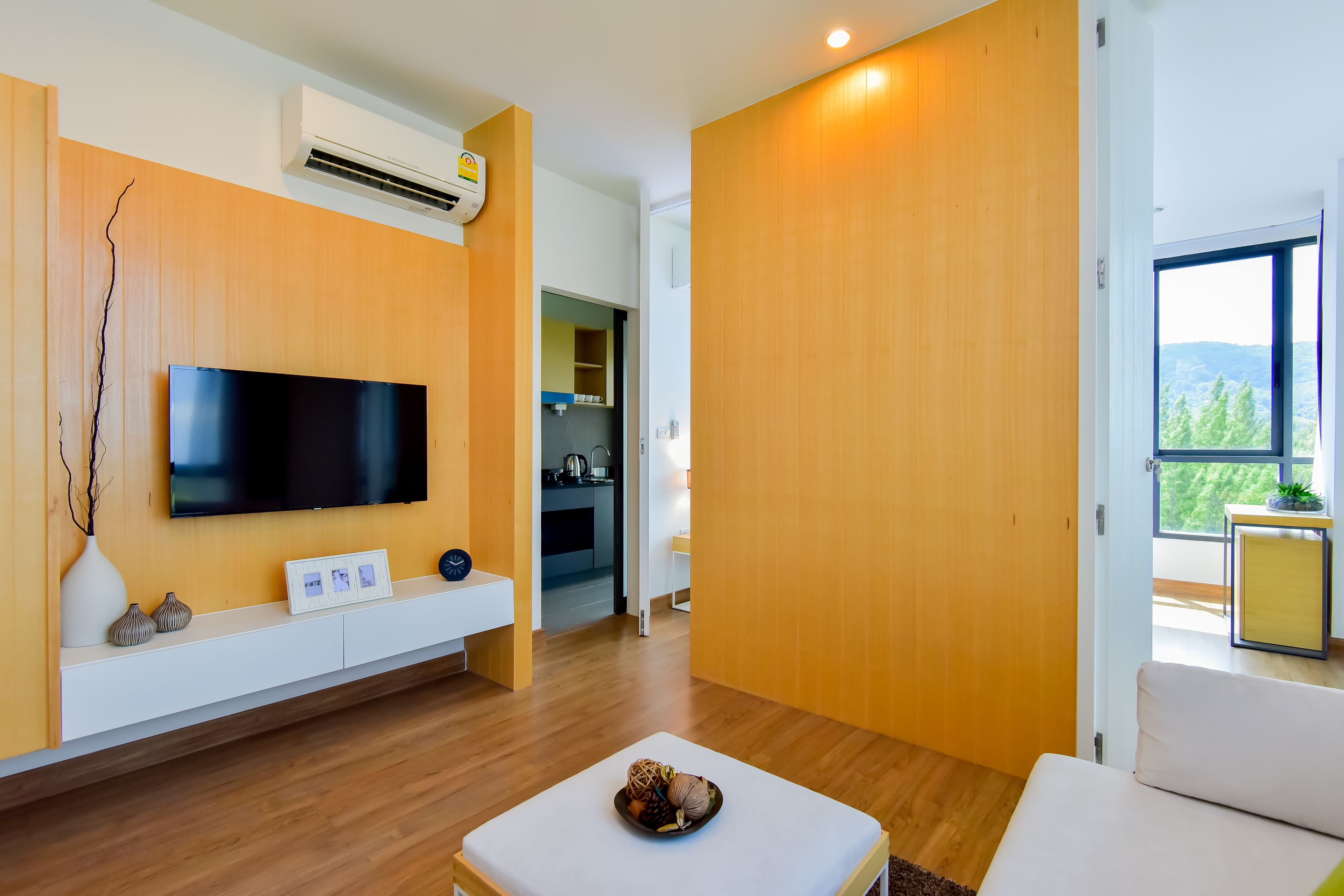 Una sala de estar moderna con un televisor de pantalla plana, paneles de madera, una consola blanca y un amplio ventanal con vistas al verdor.