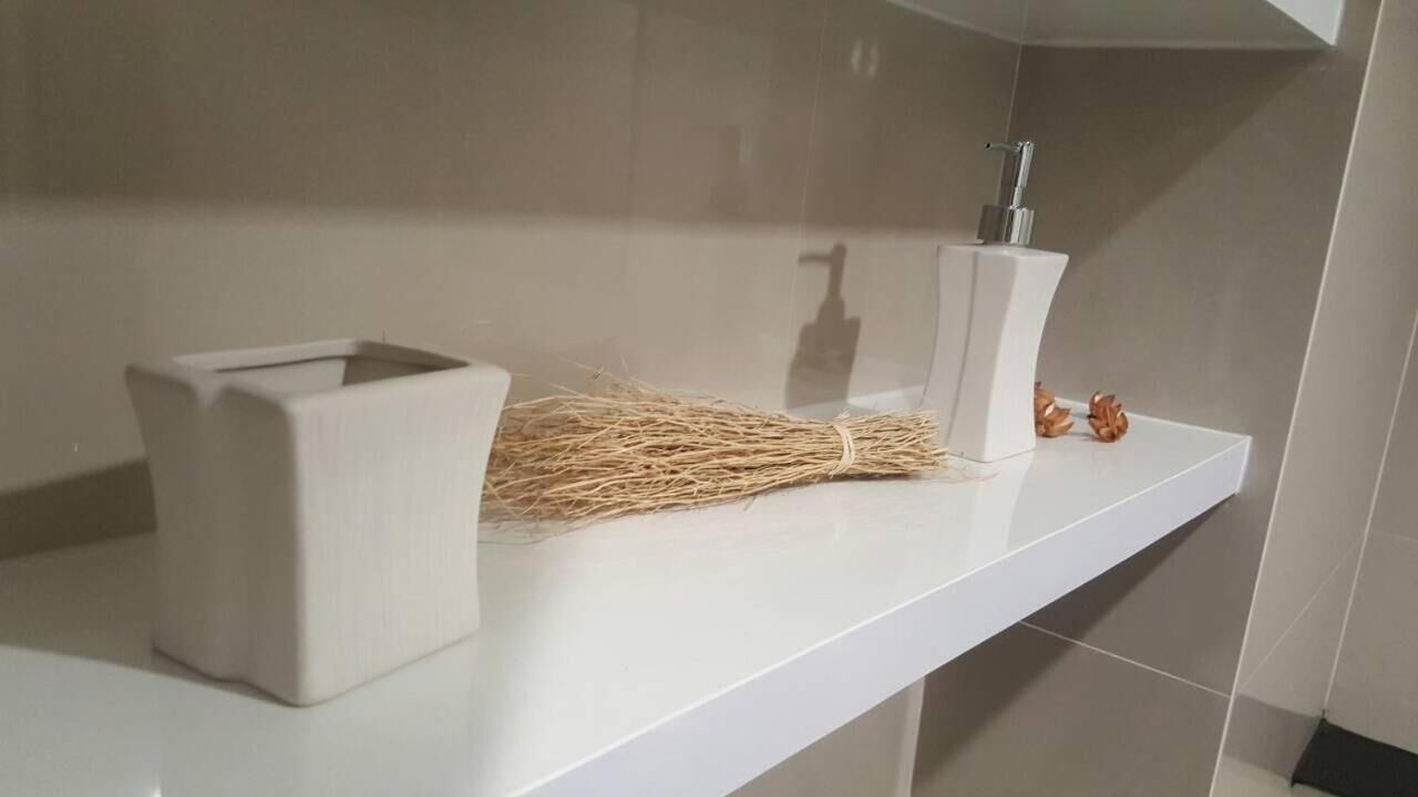 Un baño con encimera blanca, un lavabo blanco con grifo cromado y un jarrón blanco con flores secas.