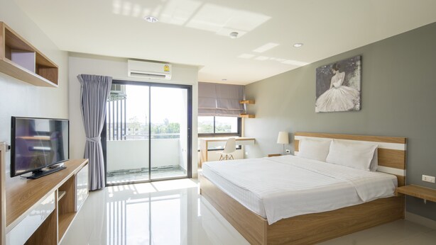 A modern hotel room with a large bed, a TV, a desk, and a balcony with curtains. - JK Living Hotel & Service Apartment (Chachoengsao)