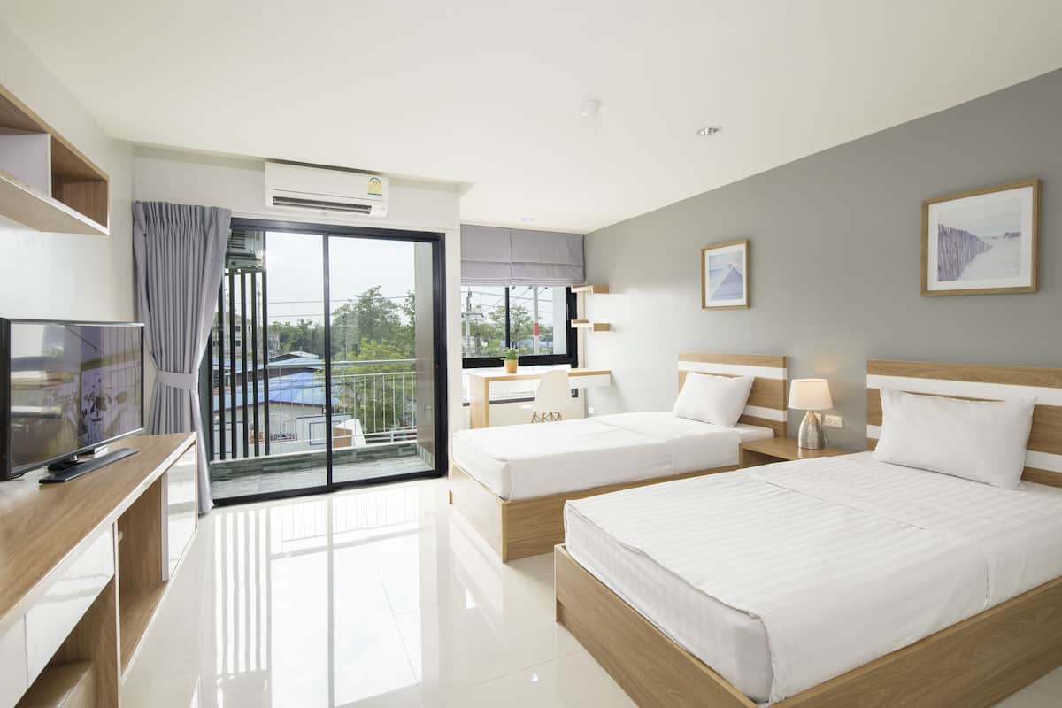 A modern hotel room with a balcony, a desk with a chair, two beds, and a TV.