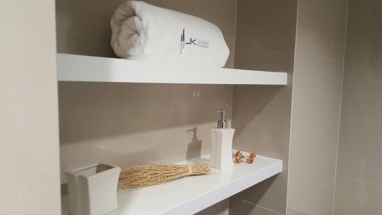 Un baño con una toalla blanca en un estante, un dispensador de jabón blanco y una escoba.