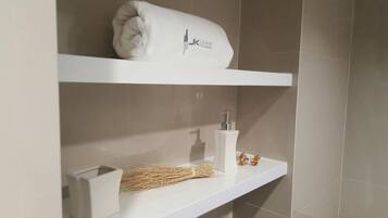 Un baño con una toalla blanca en un estante, un dispensador de jabón blanco y una escoba.