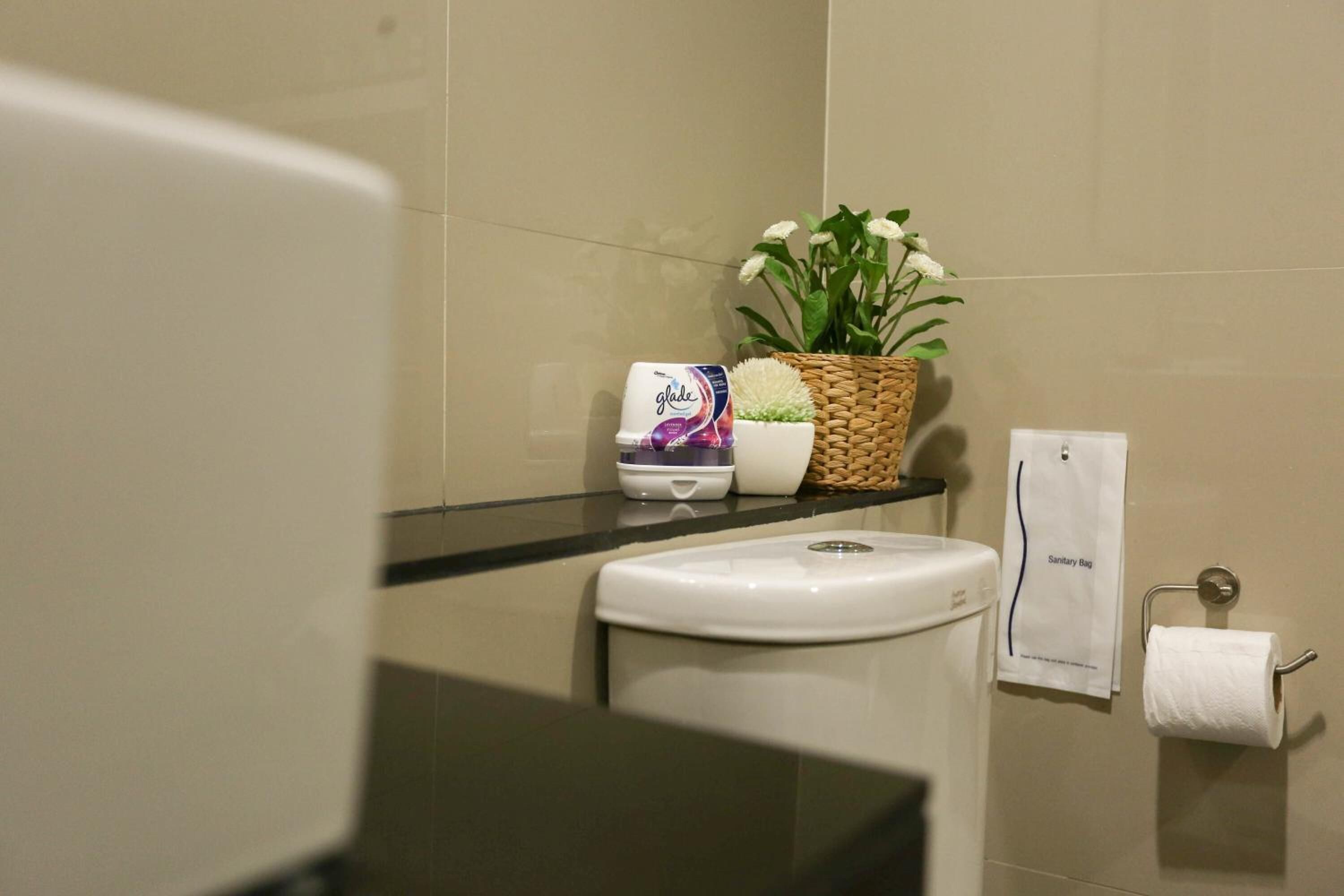 Ein Badezimmer mit Toilette, einem Korb mit Blumen, einer Lotionflasche und einer Hängentasche für Hygieneartikel an der Wand.