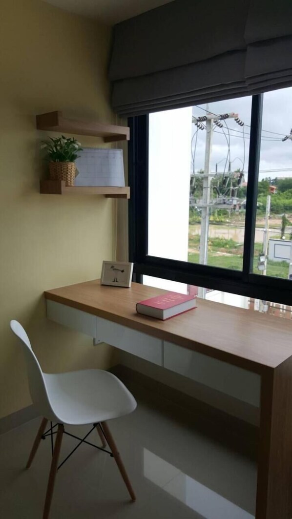 A study room with a desk, chair, and a window with a view of the outside. - JK Living Hotel & Service Apartment (Chachoengsao)