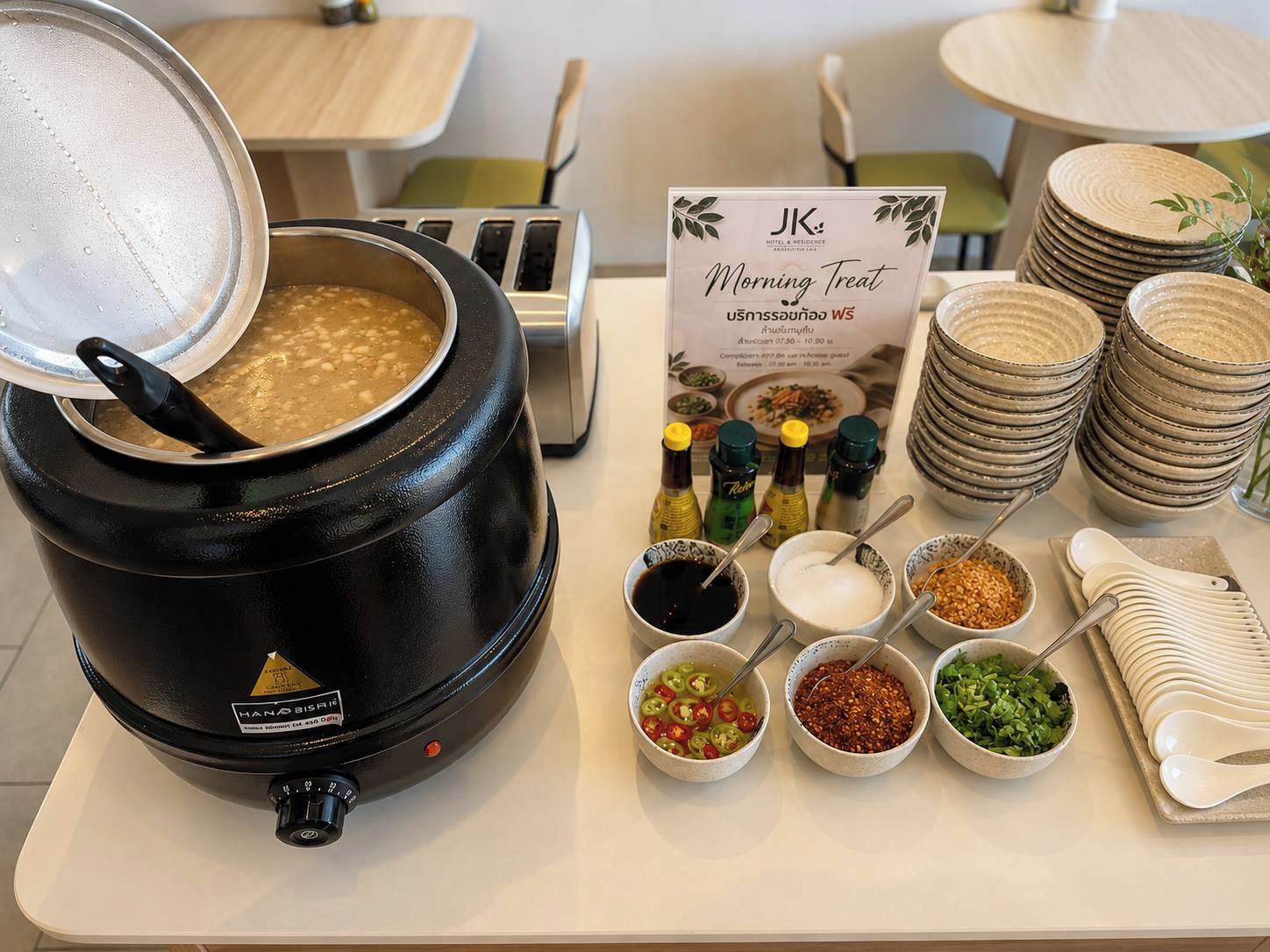 Disposición de un bufé de desayuno con una olla grande de sopa, salsas y platos apilados.