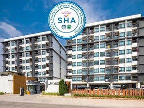 A modern multi-story residential building with balconies, a visible entrance, and a logo for "Amazing Thailand AddHealth & Safety Administration". - JK Living Hotel & Service Apartment (Chachoengsao)