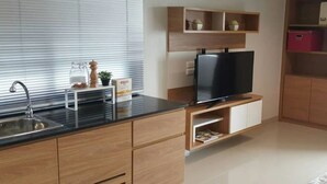 Eine moderne Küche mit integriertem Spülbecken, Holzschränken, einer schwarzen Arbeitsplatte und einem Flachbildfernseher.