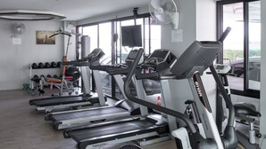 Ein Fitnessraum mit mehreren Laufbändern, einer Gewichtbank und einem Wandventilator.