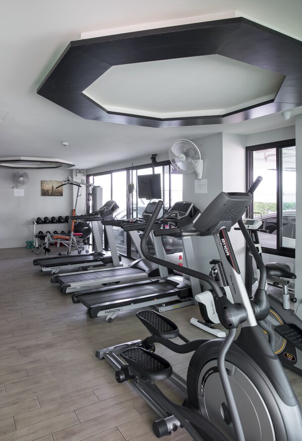 Un gimnasio con cintas de correr, una banca de pesas y un ventilador de pared.