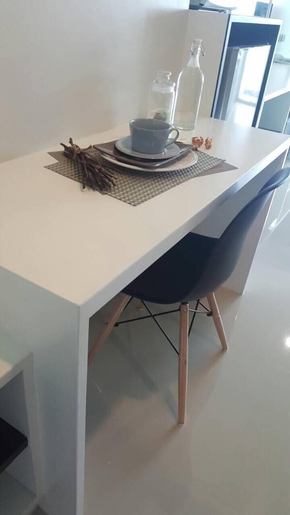 A white dining table with a placemat, a blue cup, and a bottle. - JK Living Hotel & Service Apartment (Chachoengsao)