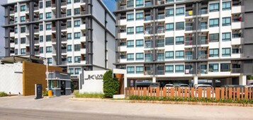 Un edificio residencial moderno de varios pisos con balcones, una entrada visible y el logotipo de "Amazing Thailand AddHealth & Safety Administration".
