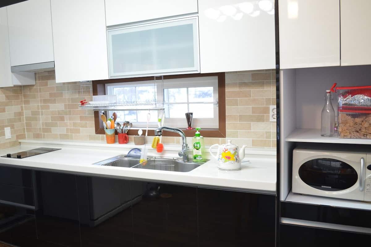 A modern kitchen with white cabinets, a stainless steel sink, a microwave, and a window above the sink.