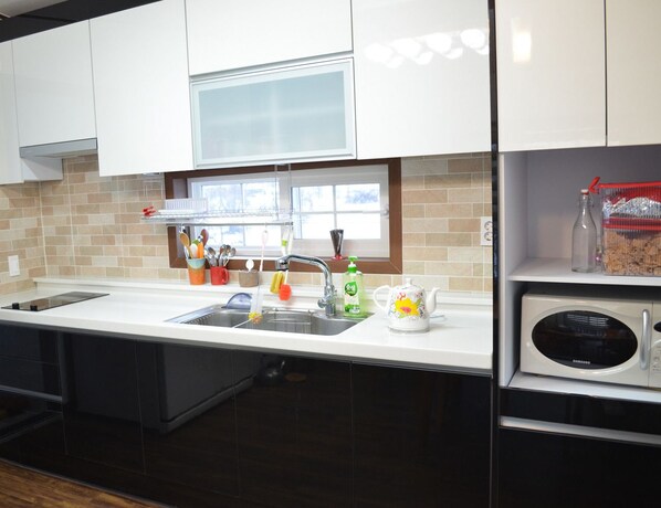Una cocina moderna con armarios blancos, un lavamanos de acero inoxidable, un microondas y una ventana sobre el lavamanos.