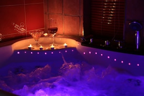 Un jacuzzi con velas y vasos, rodeado por una pared de azulejos y una ventana con persianas.