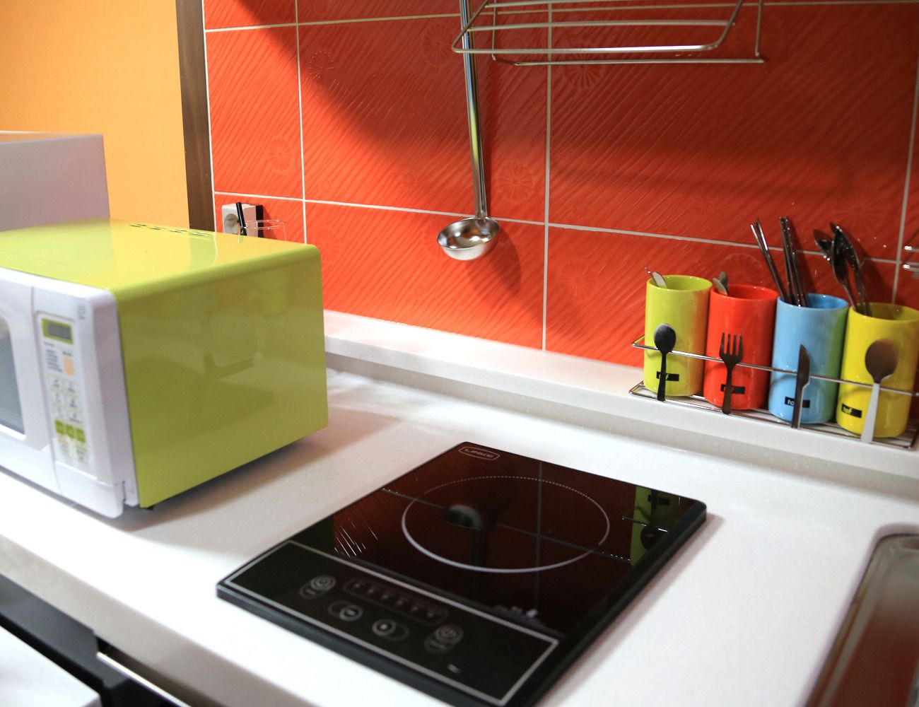 A kitchen with a microwave, an induction cooktop, and a utensil holder with colorful containers.
