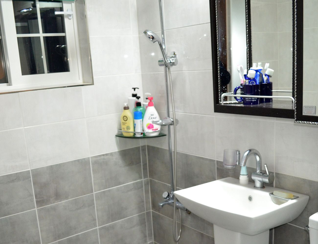 A bathroom with a white sink, a mirror, and a shower. There are toiletries on a shelf.