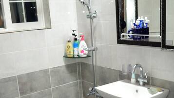 A bathroom with a white sink, a mirror, and a shower. There are toiletries on a shelf.