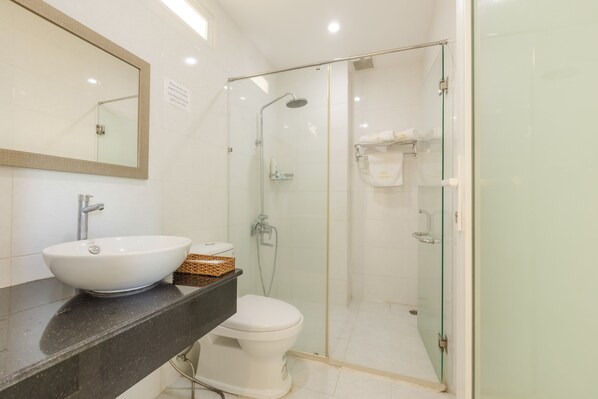 Un baño moderno con un espejo grande, un lavamanos blanco y una zona de ducha con paredes de vidrio.