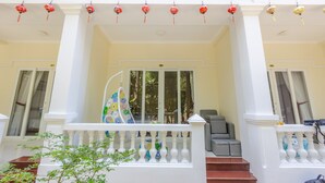 A hotel entrance with a white balustrade, a set of stairs leading up to the entrance, and a balcony with hanging decorations. - T&T Resort And Spa (Phu Quoc)