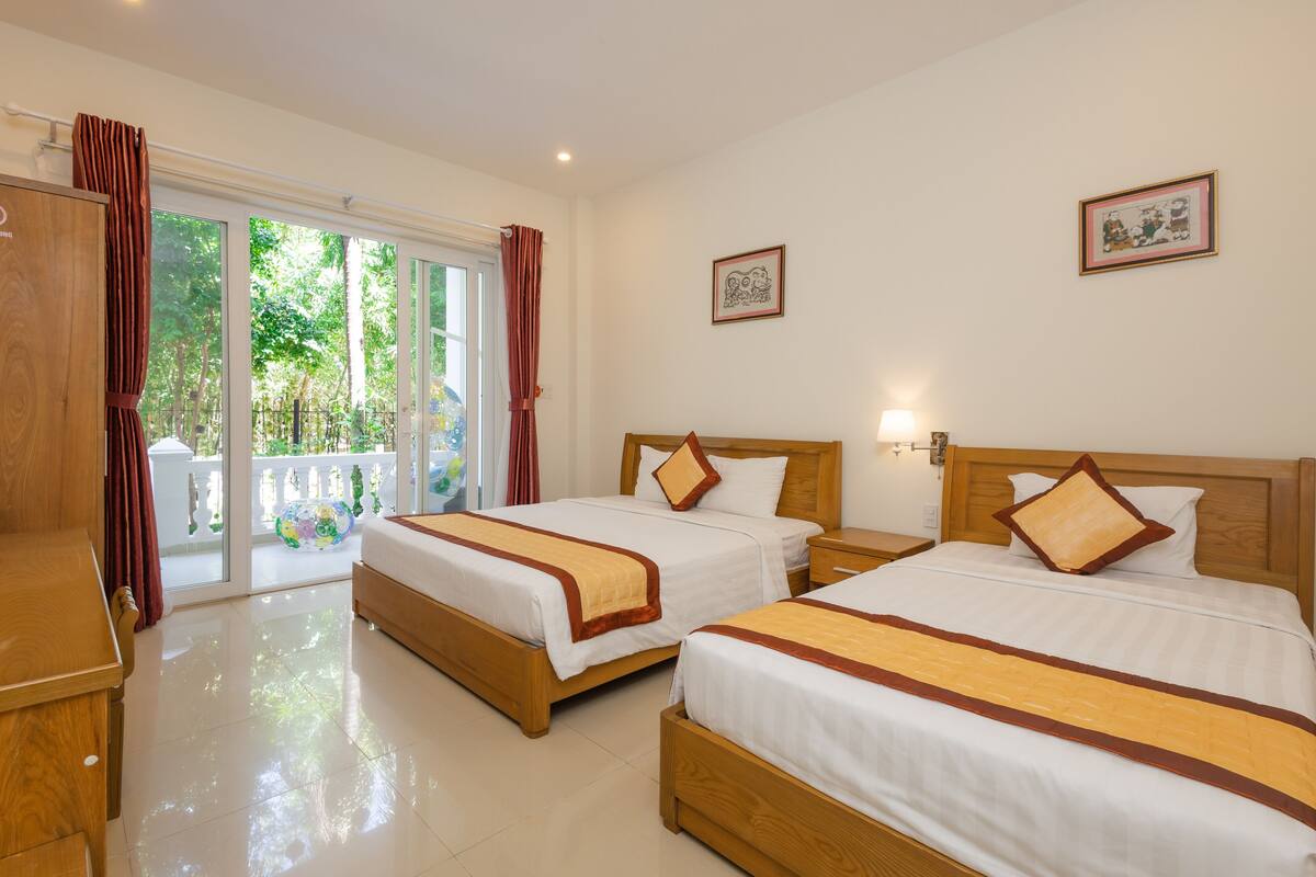 A hotel room with two beds, a wooden desk, and a balcony with curtains.