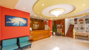 A hotel reception area with a wooden desk, two blue chairs, a clock, and a staircase. - T&T Resort And Spa (Phu Quoc)