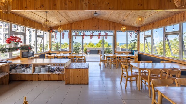 A spacious restaurant with wooden interiors, large windows, and a central seating area. - T&T Resort And Spa (Phu Quoc)