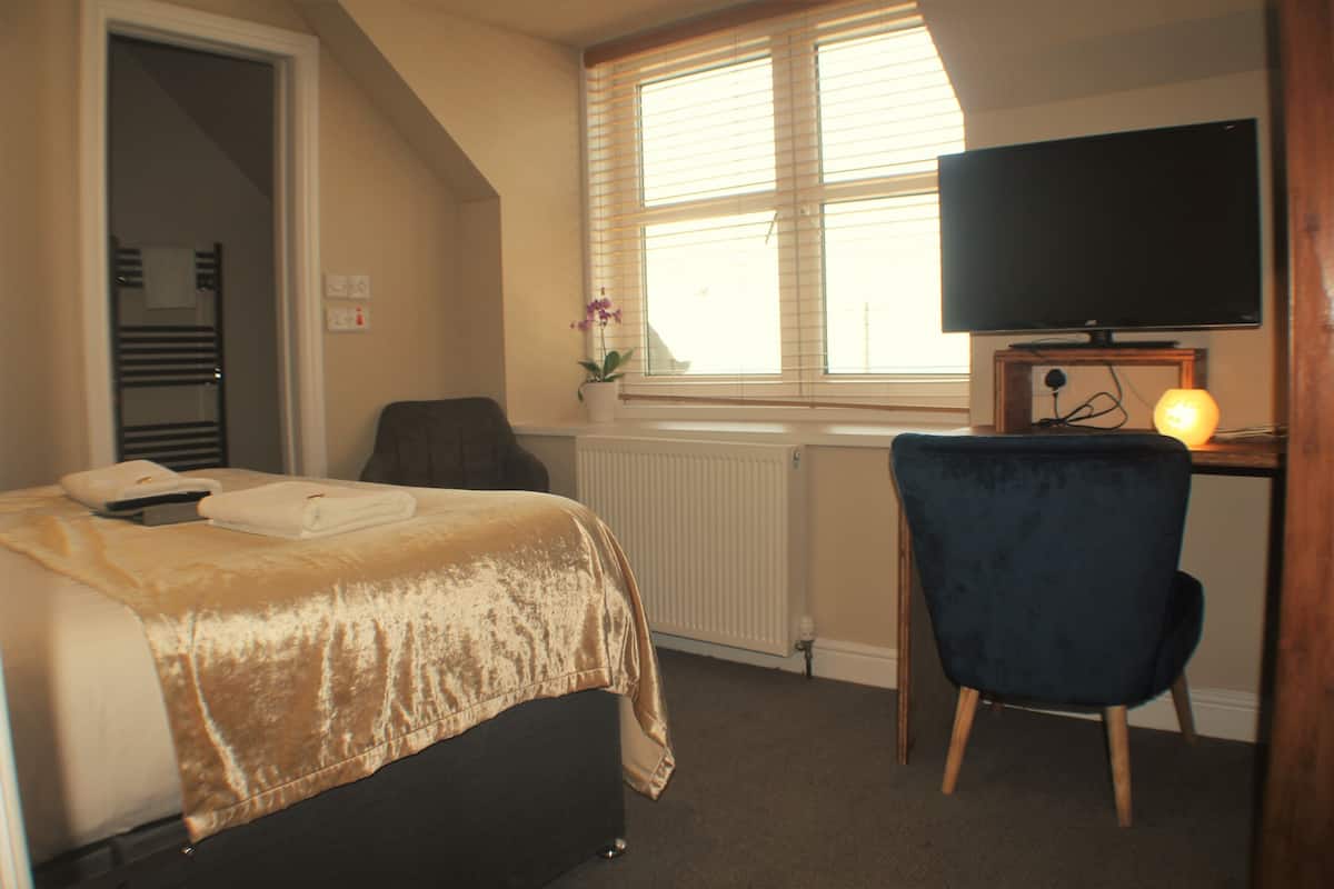A bedroom with a bed, a desk with a television, a chair, and a radiator.