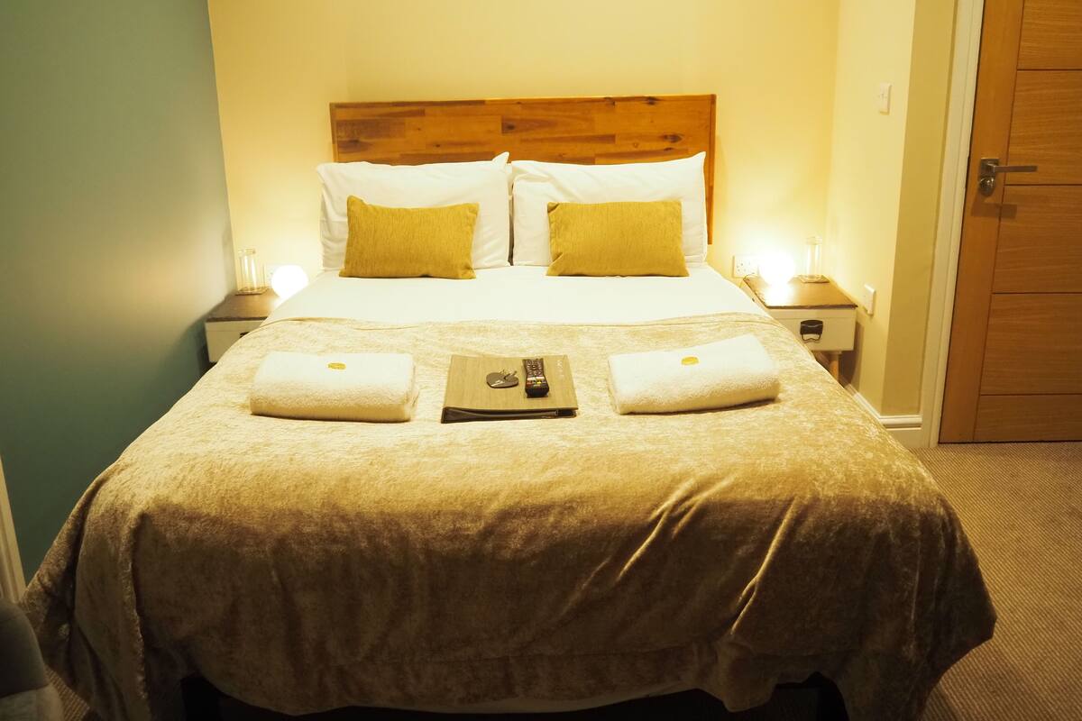 A neatly made bed with a wooden headboard, two pillows, and two folded towels on the bed.