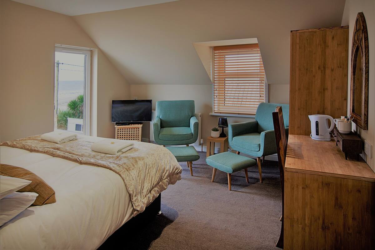 A bedroom with a bed, a television, a chair, a desk, and a wardrobe.