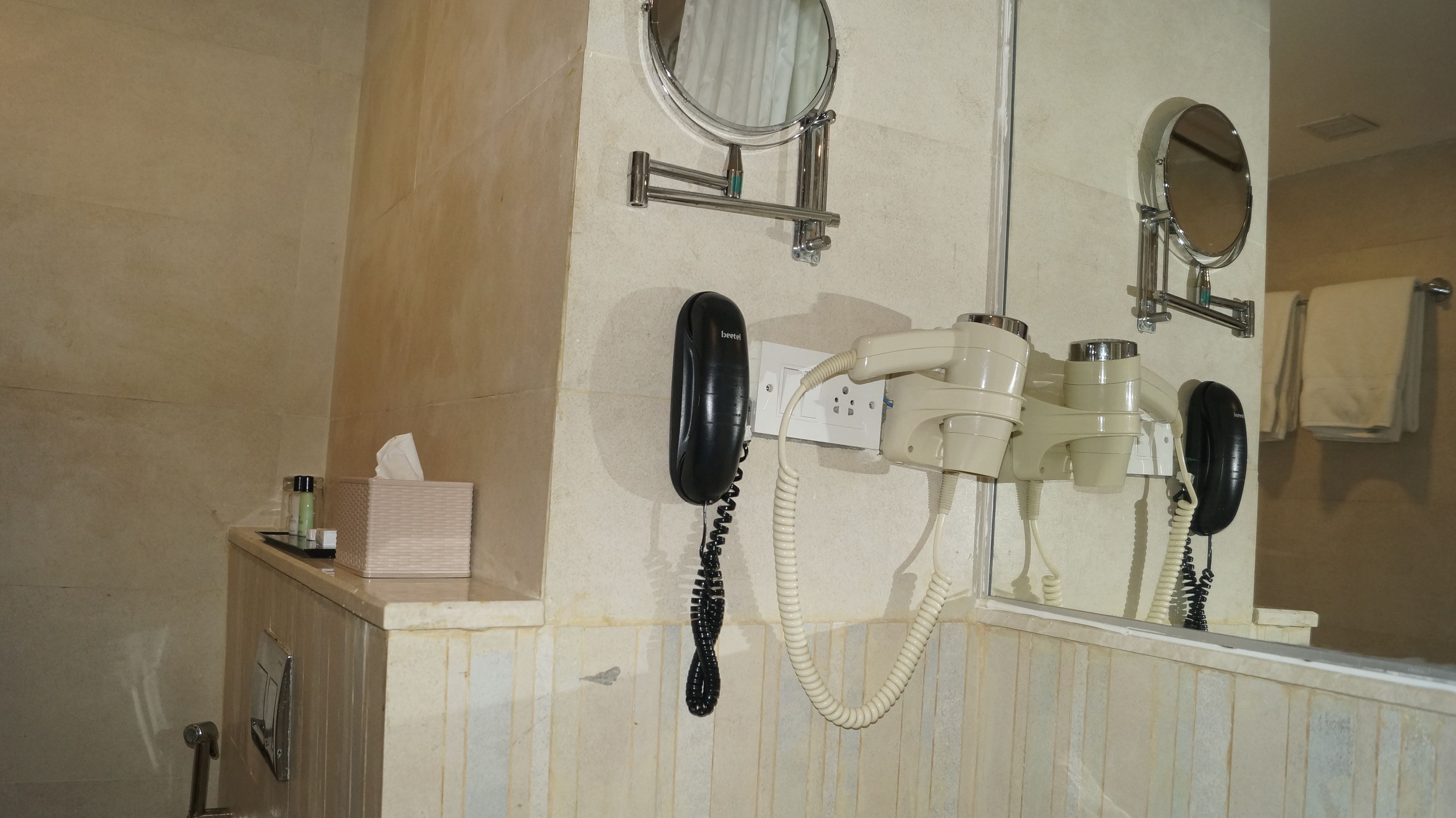 A bathroom with a mirror, a hairdryer, a telephone, and a tissue box.