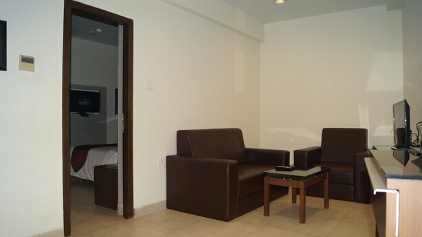 A small, modern room with two brown armchairs, a small wooden table, and a TV on a stand.