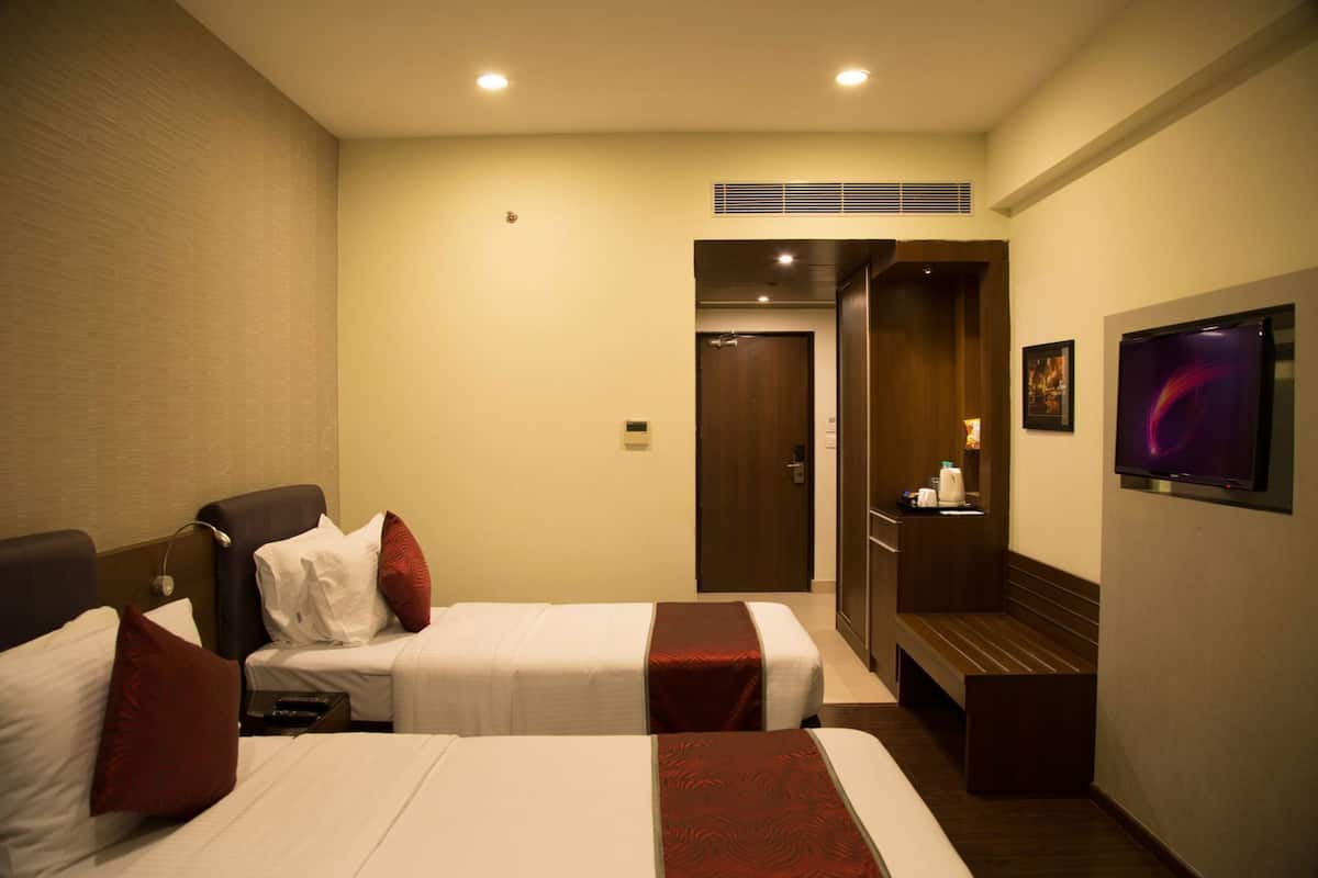 A hotel room with two beds, a TV, a mirror, and a door leading to a bathroom.