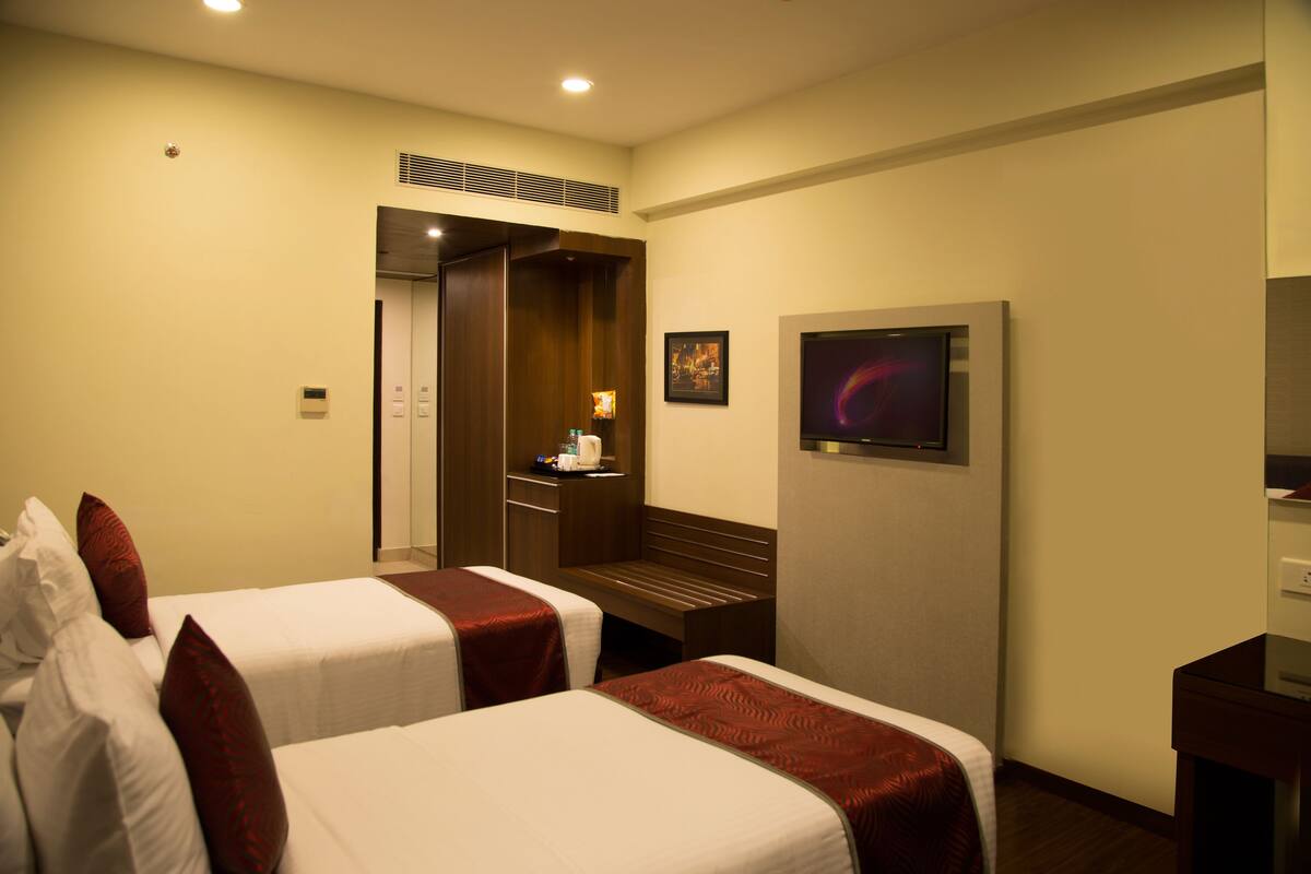 A hotel room with two beds, a desk, a chair, a television, and a door leading to a bathroom.