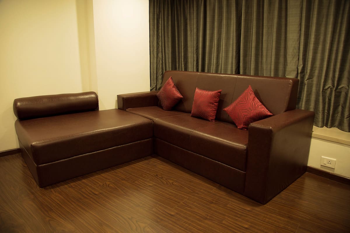 A brown leather sectional sofa with three red patterned pillows against a dark curtain backdrop.