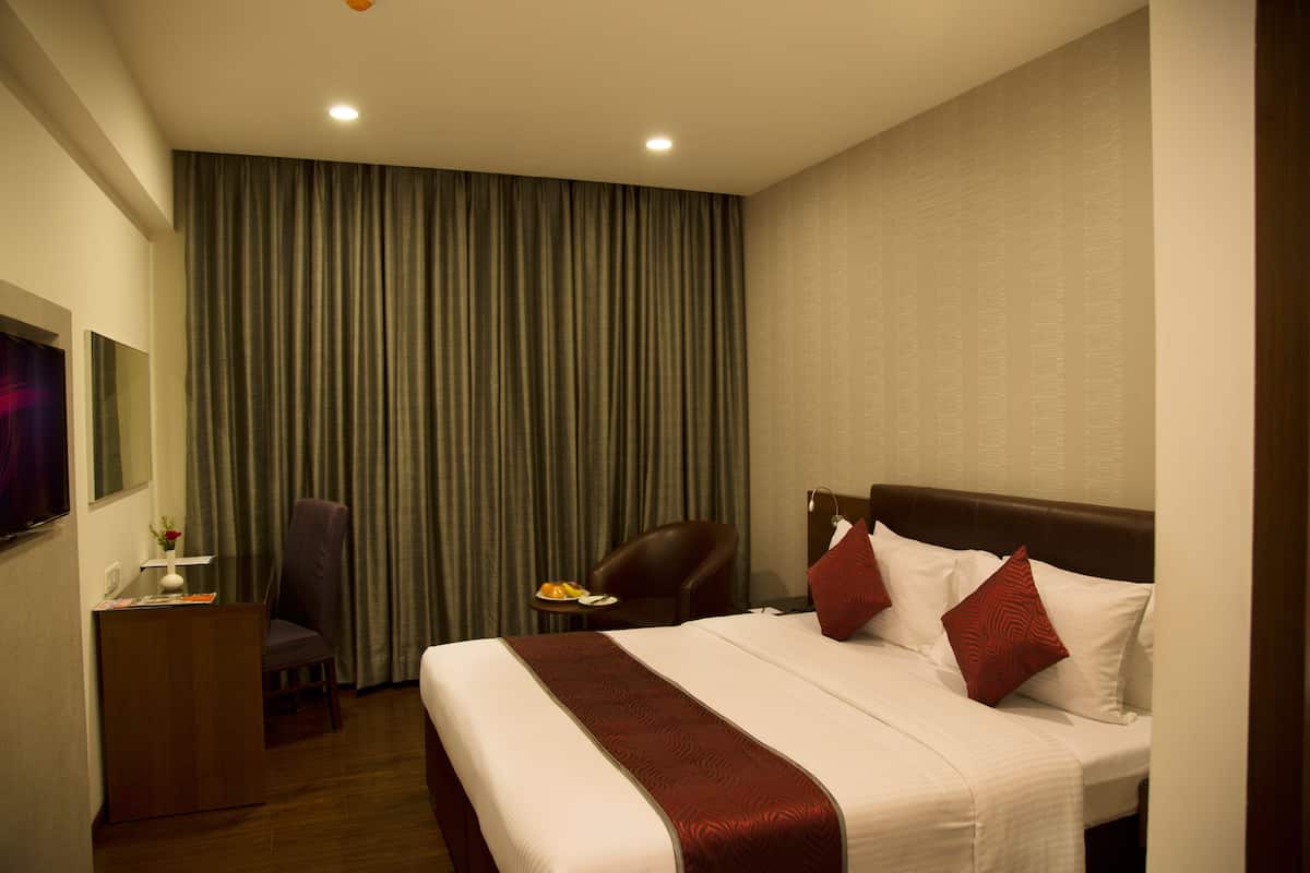 A hotel room with a bed, a desk, a chair, and a television.
