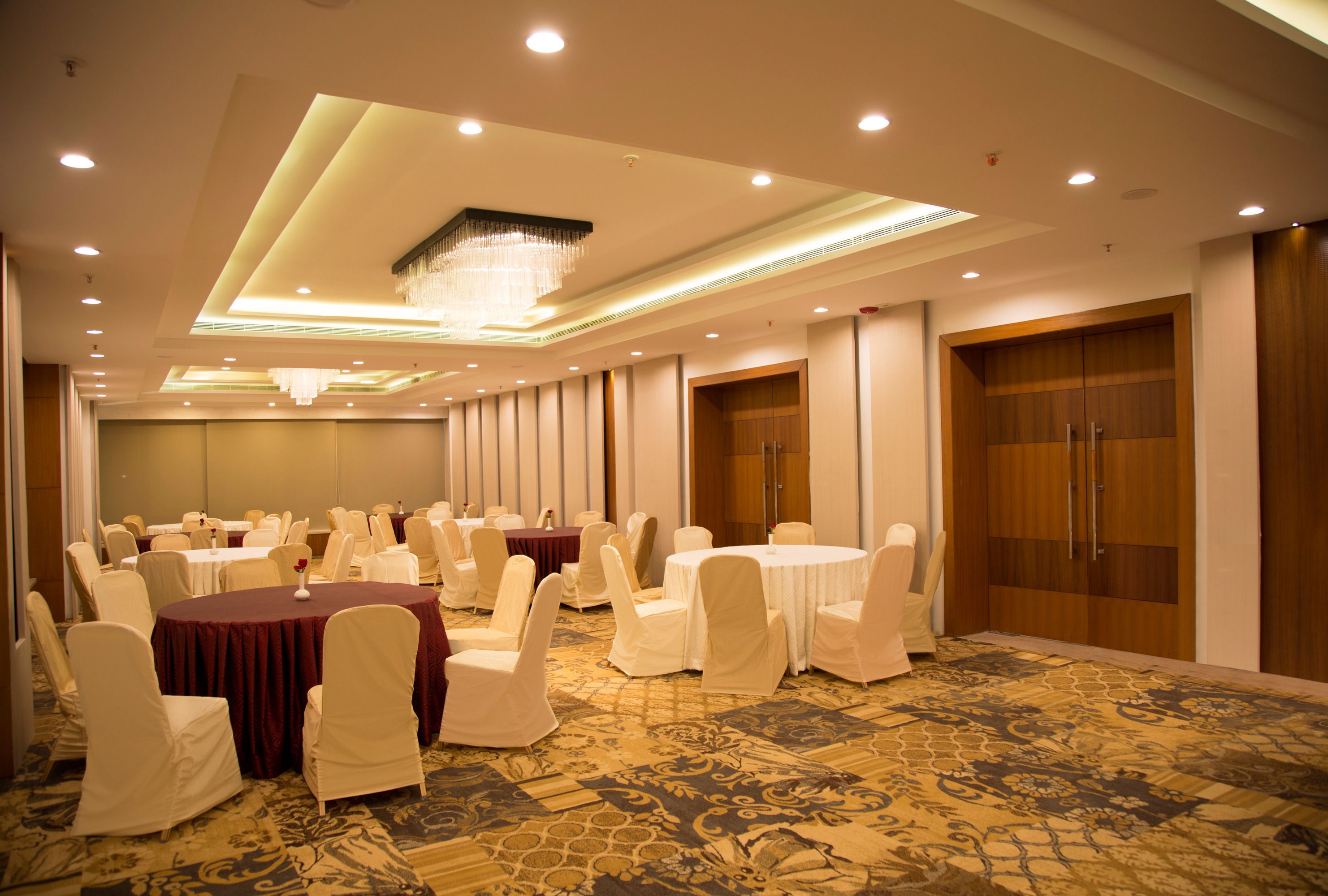 A banquet hall with round tables, white chairs, and a patterned carpet.