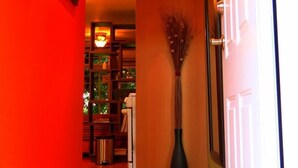 Ein Flur mit roter Wand, einer Vase mit Zweigen und einer Tür, die in einen Raum mit einem Fenster führt.