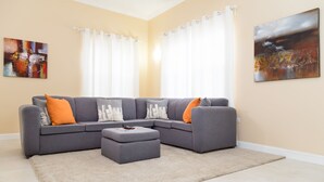 A living room with a grey sectional sofa, a small ottoman, and two paintings on the walls.