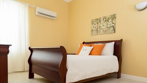 A bedroom with a wooden bed, white bedding, and two wall-mounted air conditioning units.