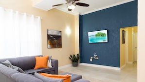 A living room with a gray sofa, a flat-screen TV mounted on a blue wall, and a ceiling fan.