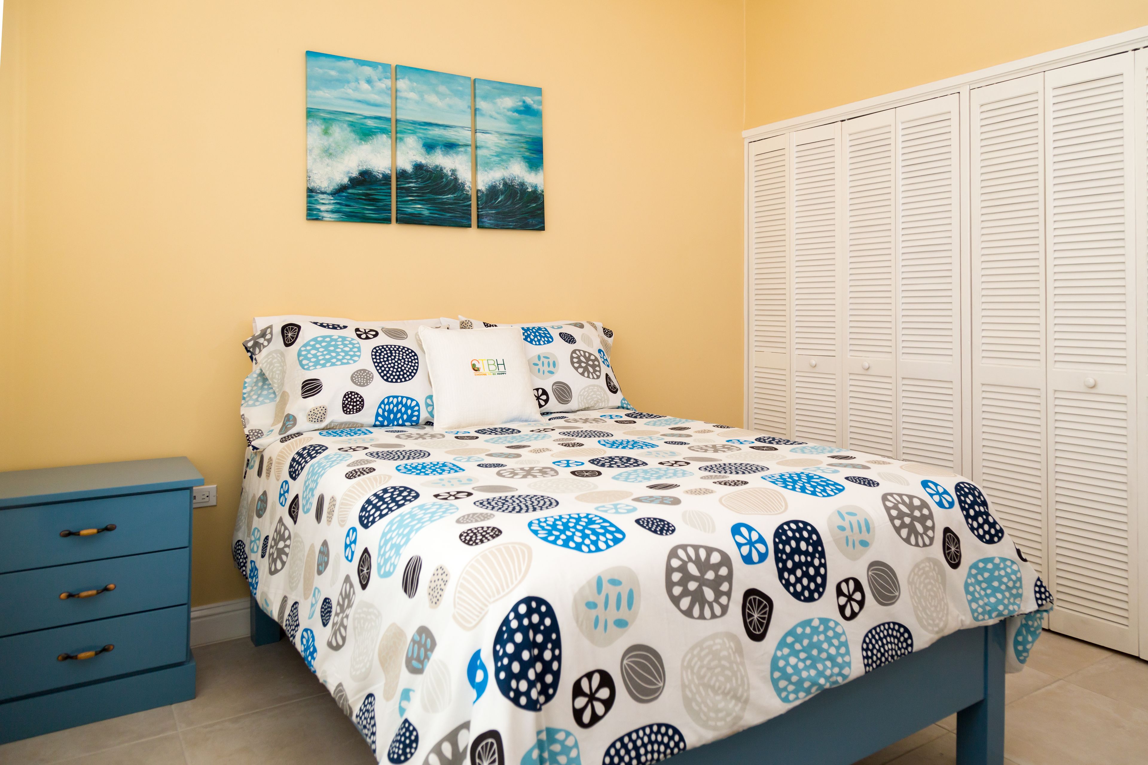 A bedroom with a bed, a nightstand, a wardrobe, and a wall with a painting.
