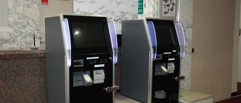 Dois quiosques de autoatendimento num saguão com paredes de mármore e uma obra de arte emoldurada acima.