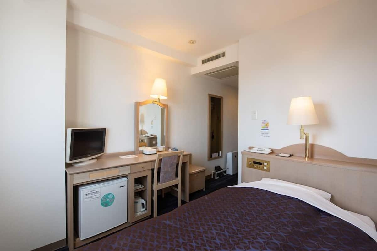 A hotel room with a bed, desk, chair, television, and a small refrigerator.