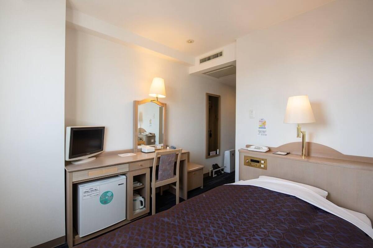 A hotel room with a bed, desk, chair, television, and a small refrigerator.