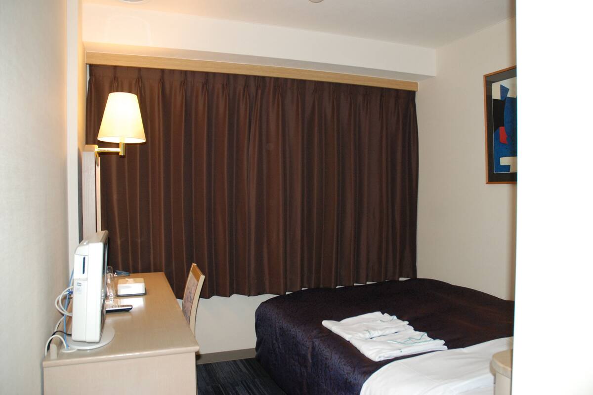 A hotel room with a bed, a desk with a lamp, and a painting on the wall.