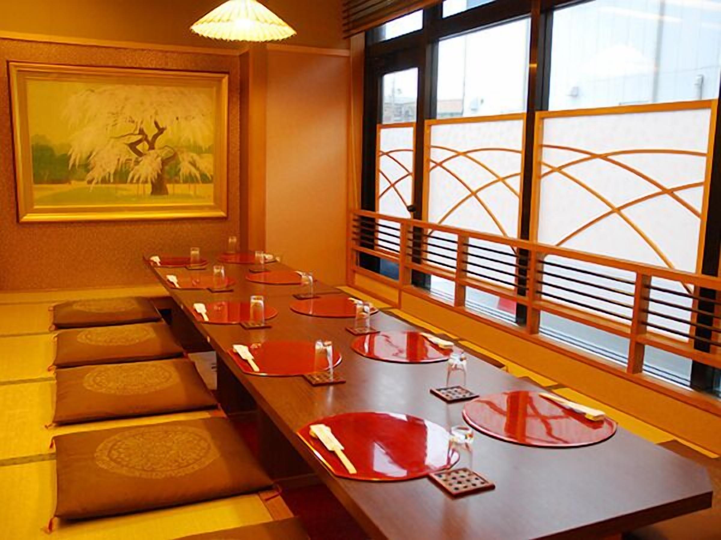A traditional Japanese-style room with tatami mats, a long table with red placemats, and a shoji screen.