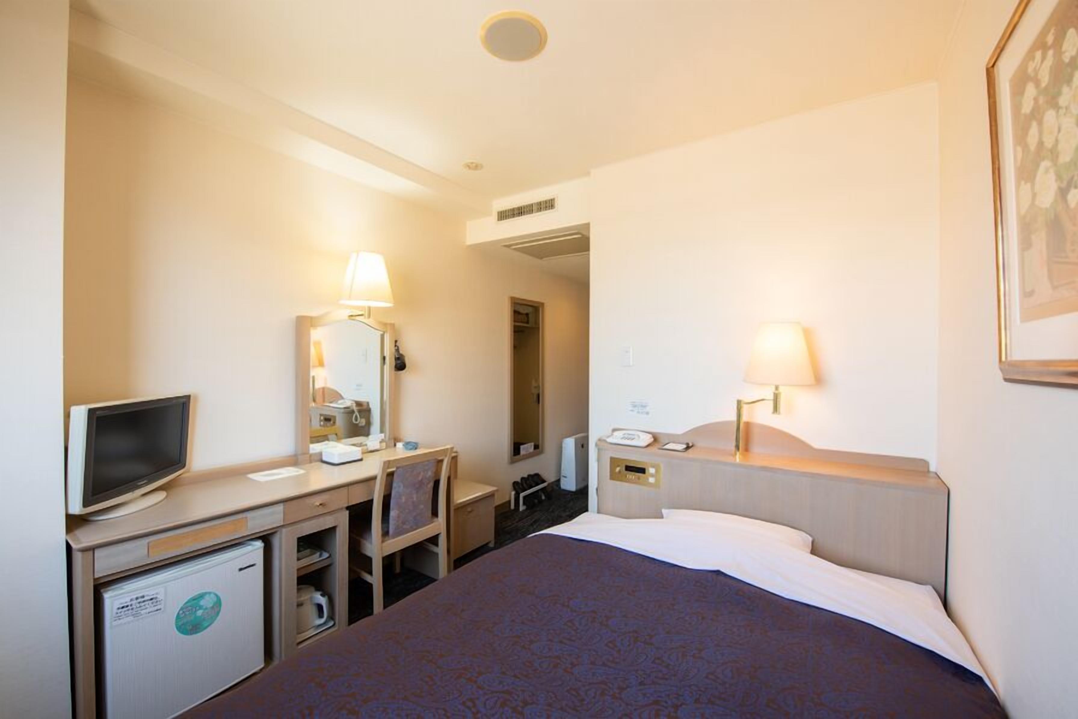 Ein Hotelzimmer mit Bett, Schreibtisch, Stuhl, Fernseher und Kühlschrank.