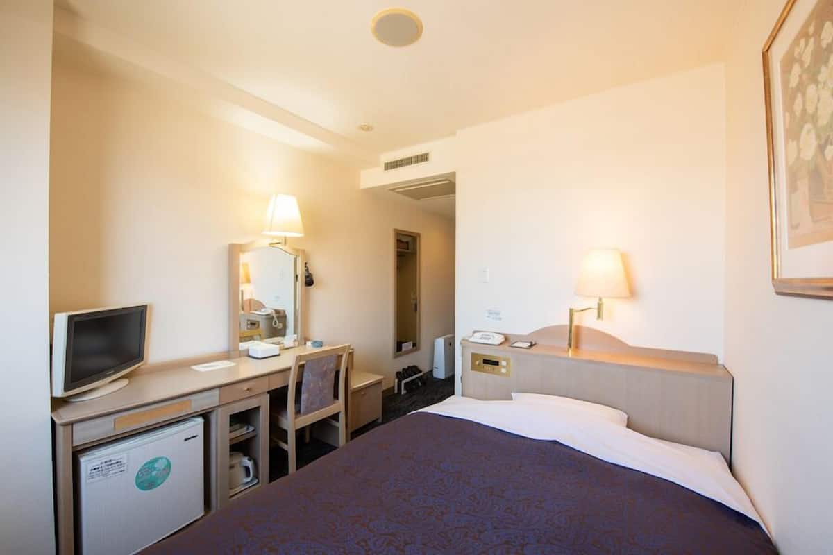 A hotel room with a bed, desk, chair, television, and a refrigerator.