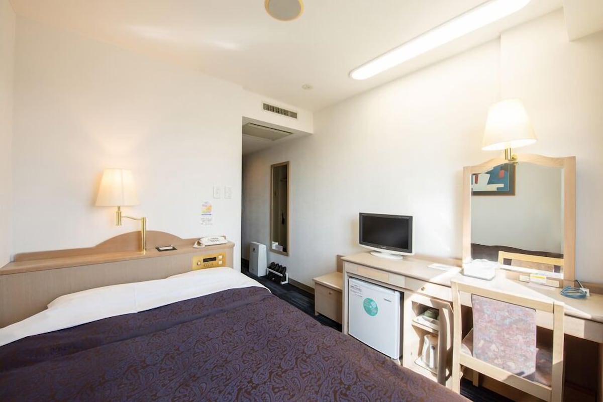 A hotel room with a bed, desk, TV, and a small refrigerator.